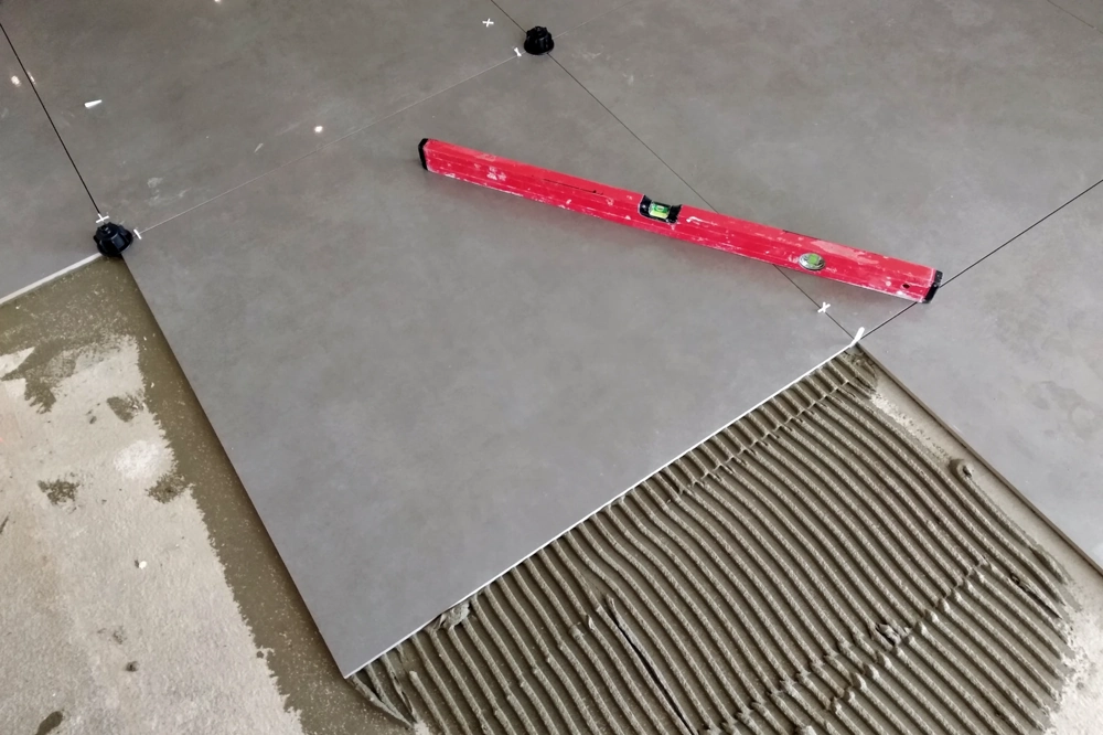 Verlegung großformatiger grauer Bodenfliesen mit Nivelliersystem und Wasserwaage