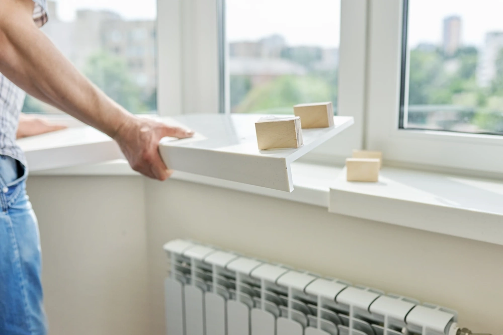 Handmontage einer weißen Fensterbank innen mit Holzkeilen über Heizkörper