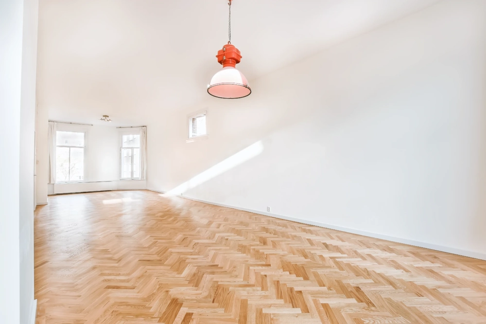 Helles, leeres Zimmer mit Fischgrät-Parkett verlegen und roter Deckenleuchte