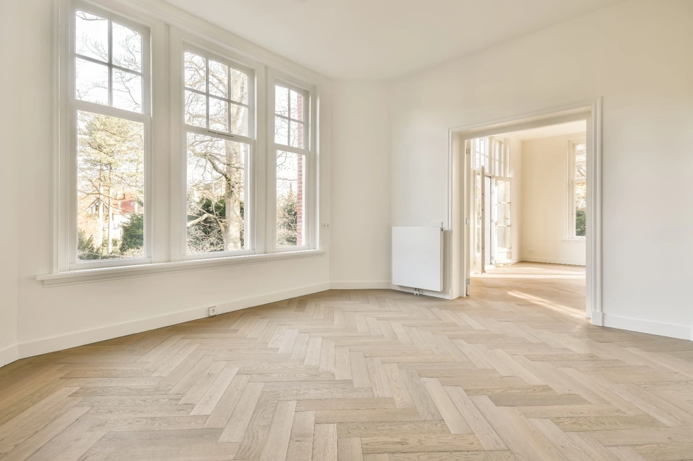 Heller, leerer Raum mit frisch verlegtem Fischgrätparkett und strahlend weißen Wänden Parkett verlegen